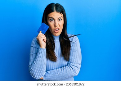 Beautiful Brunette Woman Holding Credit Card Clueless And Confused Expression. Doubt Concept. 