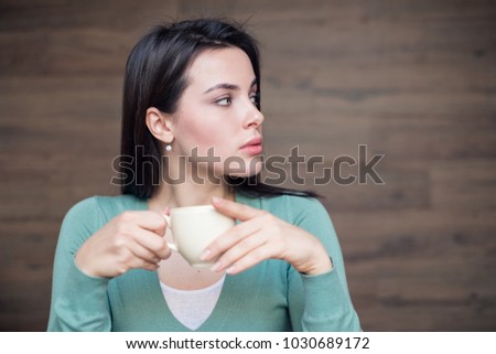 Beautiful brunette woman holding cup of coffee and looking out of camera