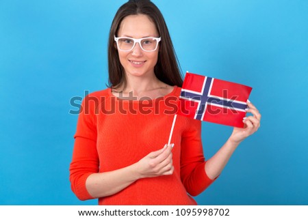 Beautiful brunette woman holding a flag of Norway standing in front of a blue background.
