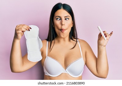 Beautiful Brunette Woman Holding Sanitary Pad And Cotton Tampon Making Fish Face With Mouth And Squinting Eyes, Crazy And Comical. 