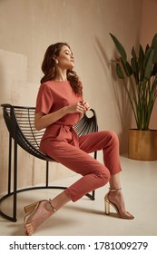 Beautiful brunette woman natural makeup wear fashion clothes casual dress code office style total pink blouse and pants suit, romantic date business meeting accessory armchair interior stairs