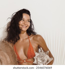 A beautiful brunette woman in an orange bikini smiles while holding a large seashell. Perfect for beach vacation, summer promo, or tropical getaway concepts. High-quality stock photo.  - Powered by Shutterstock