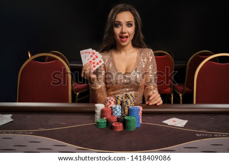 Beautiful brunette woman is playing poker sitting at the table in casino.