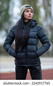Beautiful brunette woman posing at the sport stadium in jacket and hat