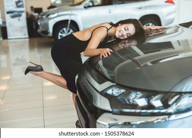 Beautiful Brunette Woman In Sexy Black Dress Feeling Happy Hugging Her Brand New Car In Dealership Center