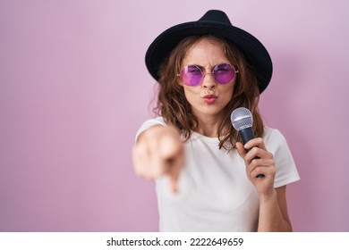 Beautiful Brunette Woman Singing Song Using Microphone Pointing With Finger To The Camera And To You, Confident Gesture Looking Serious 