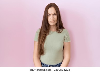 Beautiful brunette woman standing over pink background skeptic and nervous, frowning upset because of problem. negative person. 