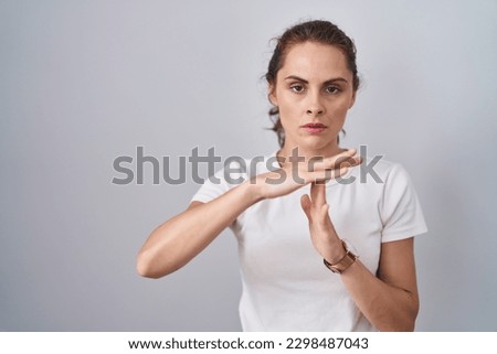 Beautiful brunette woman standing over isolated background doing time out gesture with hands, frustrated and serious face 