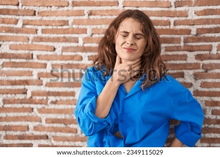 Beautiful brunette woman standing over bricks wall touching painful neck, sore throat for flu, clod and infection 