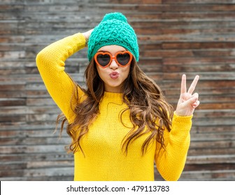 Beautiful brunette woman in sunglasses and knitted  cap blowing lips kiss over wooden background. - Powered by Shutterstock