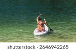 Beautiful brunette woman trains on a stand up paddle board in the lake of Levico in Trentino. The woman is thirty-eight years old and is of Caucasian origin