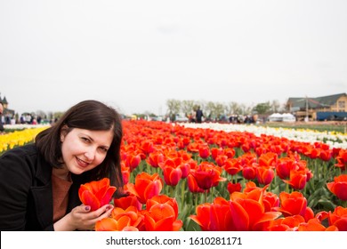 Beautiful Brunette Woman With Tulips In Field Of Flowers