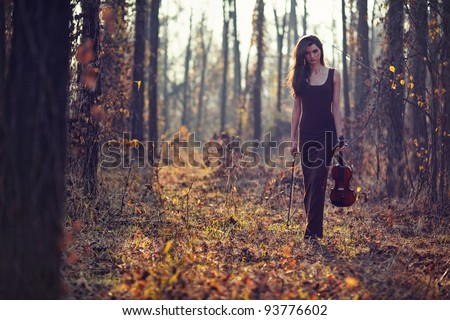 A beautiful brunette woman walking alone in a forest with a violin.