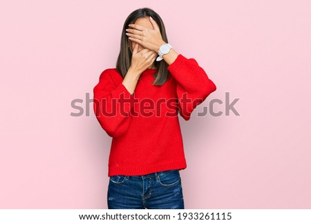 Beautiful brunette woman wearing casual winter sweater covering eyes and mouth with hands, surprised and shocked. hiding emotion 