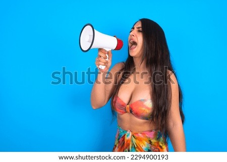 beautiful brunette woman wearing swimwear over blue background Through Megaphone with Available Copy Space