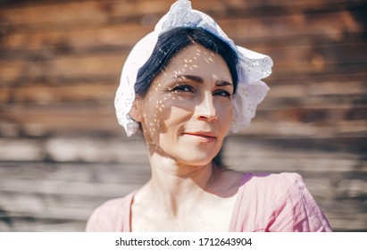 Beautiful brunette woman in a white headdress looks at the camera on a wooden background. Portrait of a young pretty woman in the sunlight. Shadow. Smile. Female. Emotion. Emotional. 
