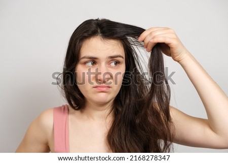 A beautiful brunette woman without makeup with dirty oily hair holds her hands on her head with a dissatisfied look