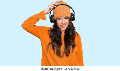 Beautiful Brunette Young Woman Listening To Music Using Headphones Confuse And Wonder About Question. Uncertain With Doubt, Thinking With Hand On Head. Pensive Concept. 