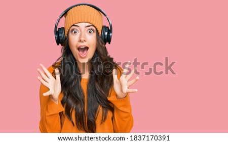 Beautiful brunette young woman listening to music using headphones celebrating crazy and amazed for success with arms raised and open eyes screaming excited. winner concept 