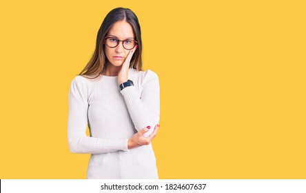 Beautiful brunette young woman wearing casual white sweater and glasses thinking looking tired and bored with depression problems with crossed arms. 