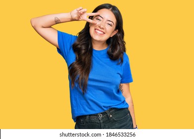 Beautiful Brunette Young Woman Wearing Casual Clothes Doing Peace Symbol With Fingers Over Face, Smiling Cheerful Showing Victory 