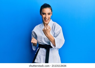 Beautiful brunette young woman wearing karate fighter uniform with black belt doing attack pose smiling and laughing hard out loud because funny crazy joke. 