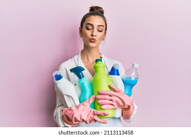 Beautiful Brunette Young Woman Wearing Cleaner Apron Holding Cleaning Products Looking At The Camera Blowing A Kiss Being Lovely And Sexy. Love Expression. 