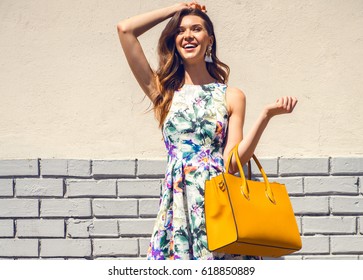 Beautiful Brunette Young Woman Wearing Nice Dress, Yellow Handbag, Walking On The Street. Fashion City Photo. Flower Pattern