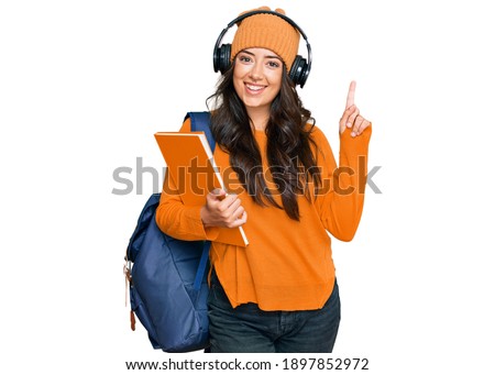 Beautiful brunette young woman wearing student backpack and holding books surprised with an idea or question pointing finger with happy face, number one 