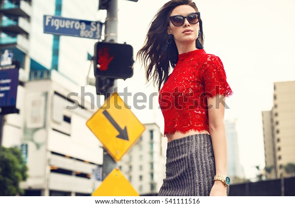 Beautiful brunette young woman\
wearing red top silver skirt and walking on the street. Fashion\
photo