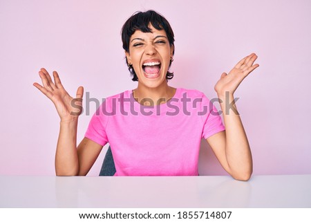 Beautiful brunettte woman wearing casual clothes over pink background celebrating mad and crazy for success with arms raised and closed eyes screaming excited. winner concept 