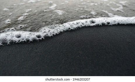 Beautiful bubbles of white sea with black sand.