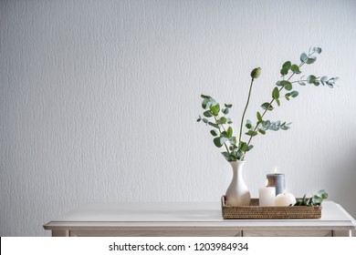 Beautiful burning candles with green leaves in vase on white table