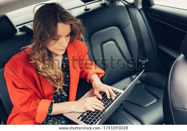 Beautiful business\
blonde woman typing on laptop in interior of the car. Working from\
vehicle. Top view\
