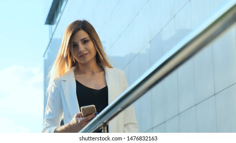 Beautiful business lady is reading a message in a smartphone. She is looking at the camera and smiling. - Shutterstock ID 1476832163