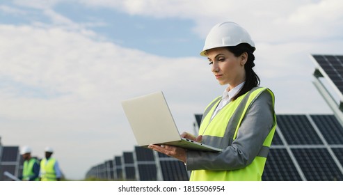 Beautiful business lady standing among field of solar panels in special uniform. Female engineer uses laptop to work outside. - Shutterstock ID 1815506954