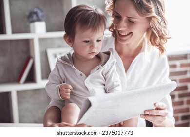 Beautiful business mom in suit is reading a newspaper with her cute baby boy and smiling, at home - Powered by Shutterstock