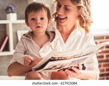 Beautiful business mom in suit is reading a newspaper with her cute baby boy and smiling, at home - Powered by Shutterstock