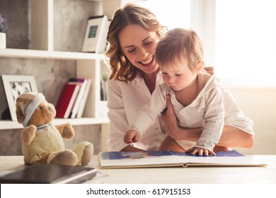 Beautiful Business Mom In Suit Is Reading A Book With Her Cute Baby Boy And Smiling, At Home