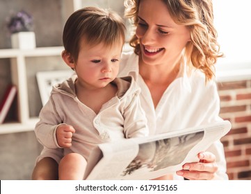 Beautiful business mom in suit is reading a newspaper with her cute baby boy and smiling, at home - Powered by Shutterstock