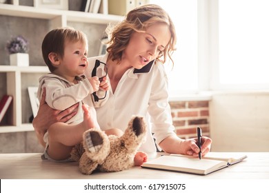 Beautiful business mom is talking on the mobile phone and taking notes while spending time with her cute baby boy at home - Shutterstock ID 617915075
