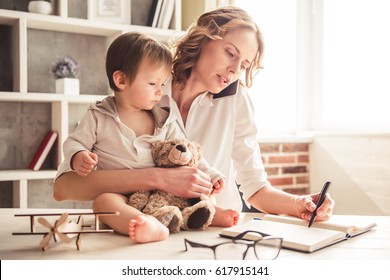 Beautiful business mom is talking on the mobile phone and taking notes while spending time with her cute baby boy at home - Shutterstock ID 617915141