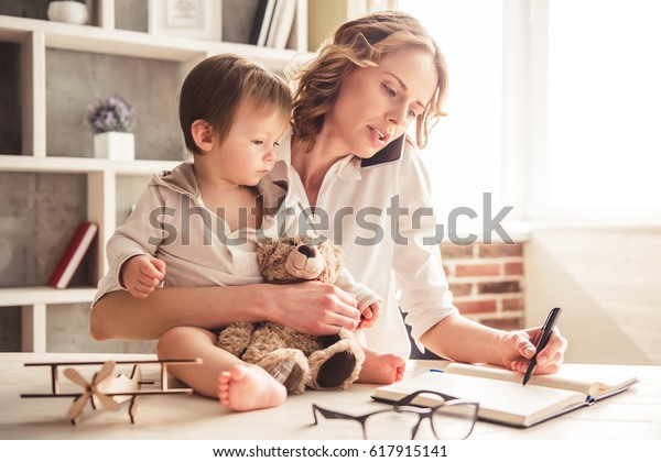 Beautiful\
business mom is talking on the mobile phone and taking notes while\
spending time with her cute baby boy at\
home