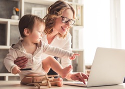 Beautiful Business Mom Is Using A Laptop And Smiling While Spending Time With Her Cute Baby Boy At Home