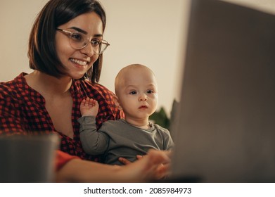 Beautiful business mom using a laptop and smiling while spending time with her cute baby boy at home - Powered by Shutterstock