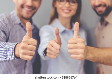 Beautiful Business People Are Showing Ok Signs, Looking At Camera And Smiling, Standing On Gray Background