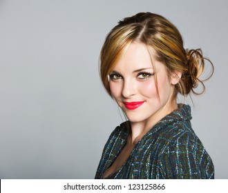 Beautiful Business Woman With Blond Hair In A Bun Wearing A Tweed Jacket And Red Lipstick On Grey Studio Background