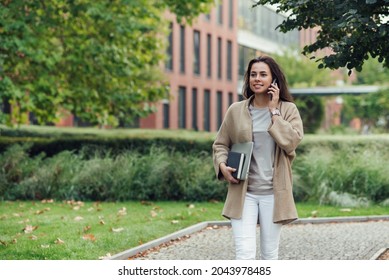 Beautiful Business Woman In Casual Outfit With A Laptop And Notebook Outdoor Speaks On Smartphone.