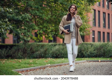 Beautiful Business Woman In Casual Outfit With A Laptop And Notebook Outdoor Speaks On Smartphone.