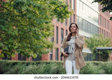 Beautiful Business Woman In Casual Outfit With A Laptop And Notebook Outdoor Speaks On Smartphone.